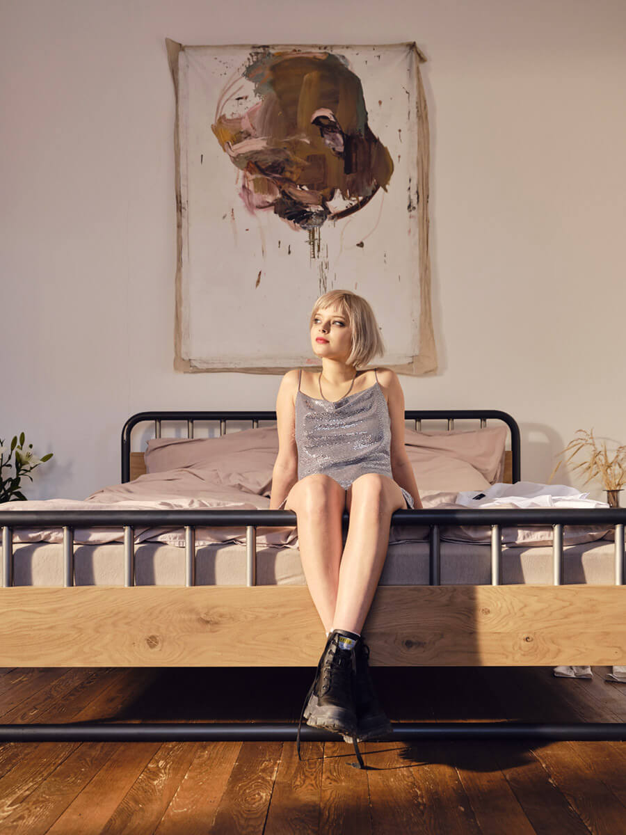 Designer Bett in Echtholz und Stahl im industrial Design auf dem eine blonde Frau sitzt.